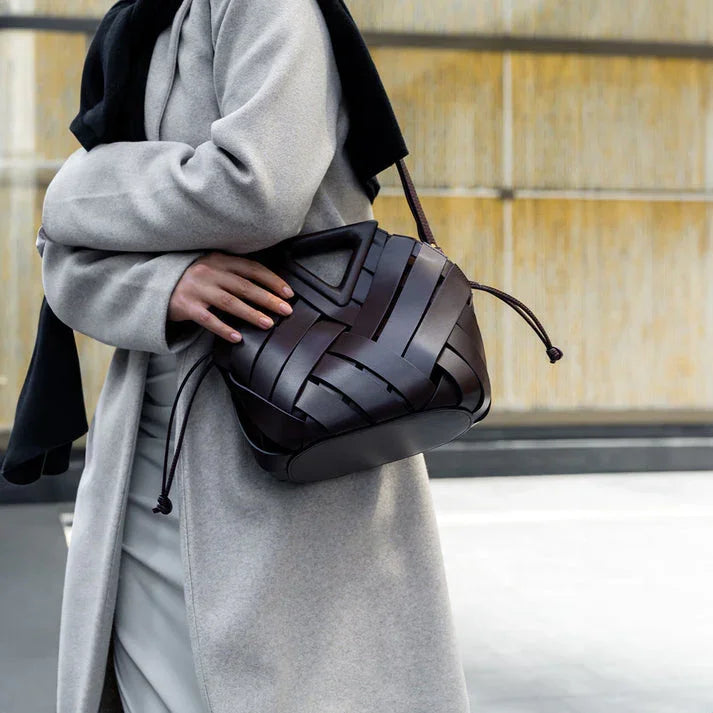 Woman in gray coat carrying a black woven leather shoulder bag with drawstring closure