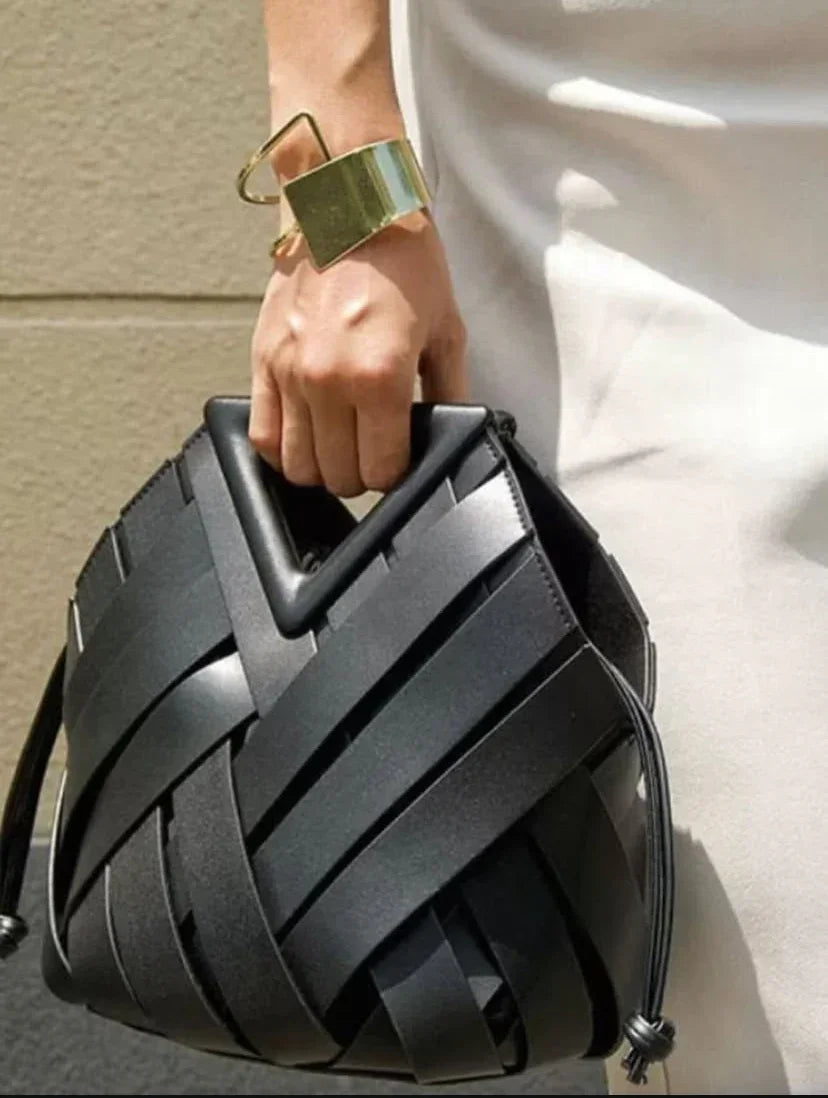 Hand holding black woven leather handbag with geometric handle and gold bracelet