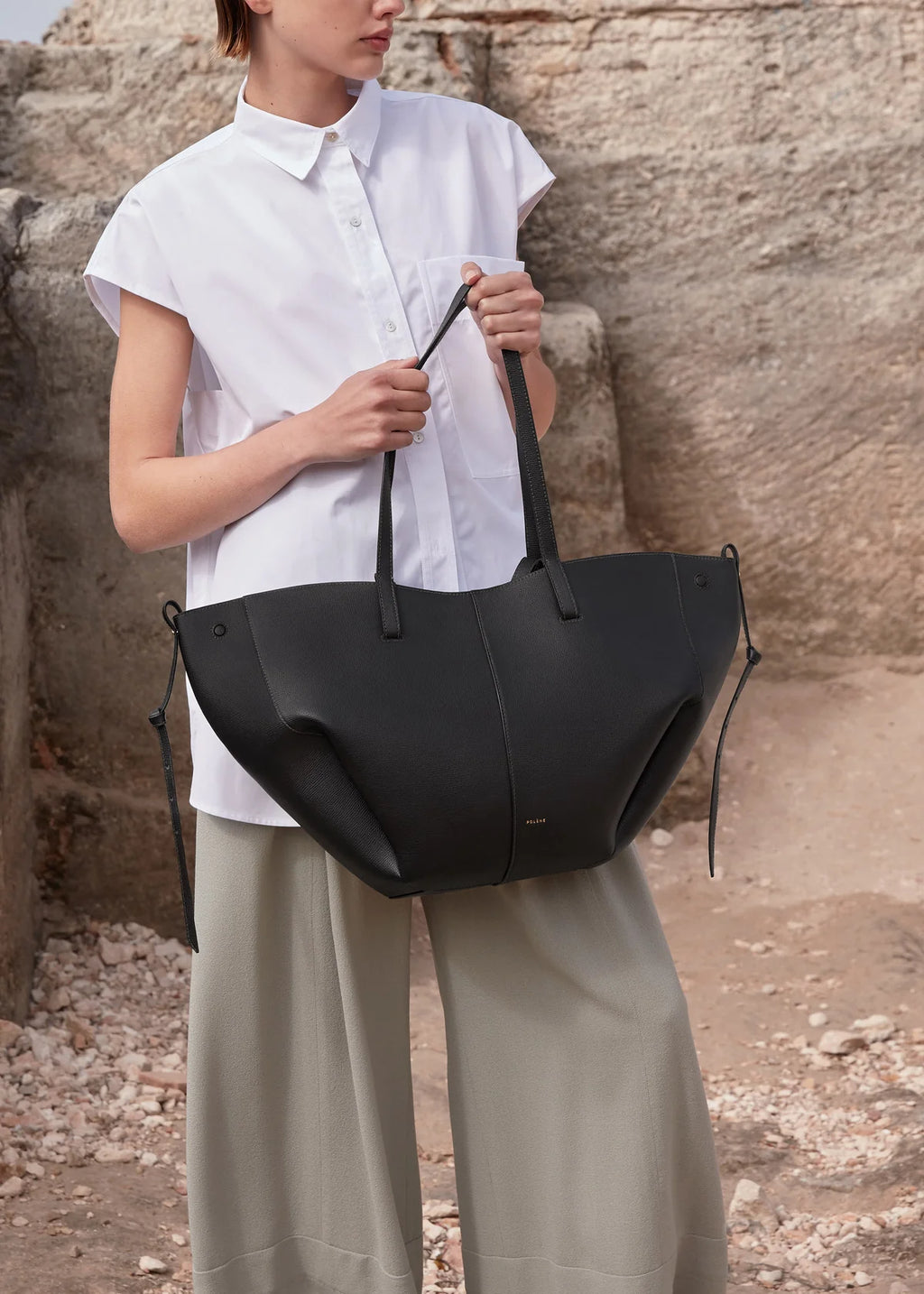 Person holding a black tote bag against a stone wall background